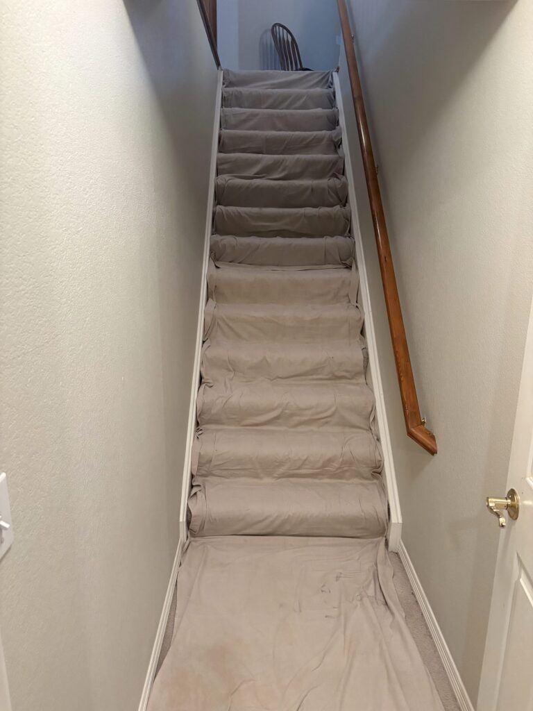 Canvas tarps covering a carpeted staircase and the hallway floor before a sewer cleaning job