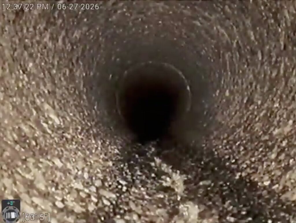 Camera view down a concrete sewer line where the cement has worn away and the whole bore is rough exposed aggregate.
