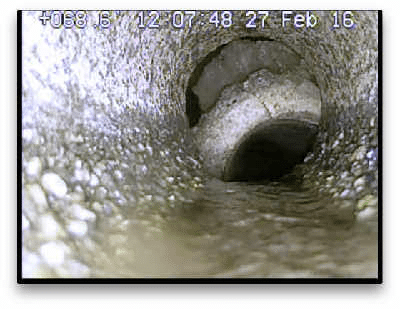 Sewer camera still of a true offset in concrete pipe with soil visible above the separated joint